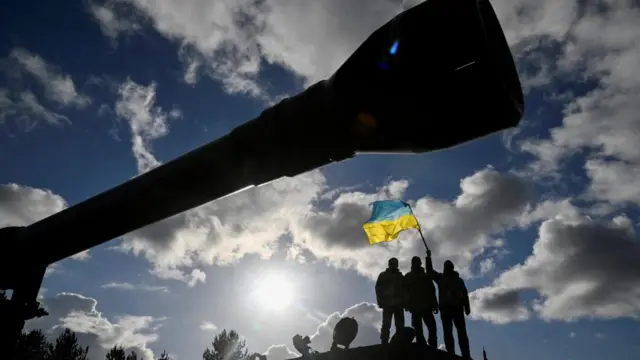 Ukrainian personnel hold a Ukrainian flag as they stand on a Challenger 2 tank during training at Bovington Camp, near Wool in southwestern Britain