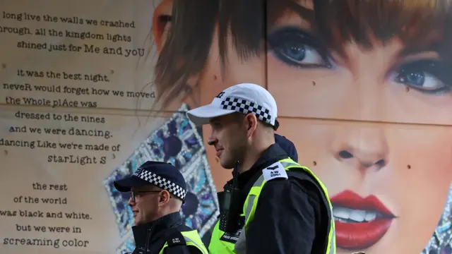 Police walk past a Taylor Swift poster