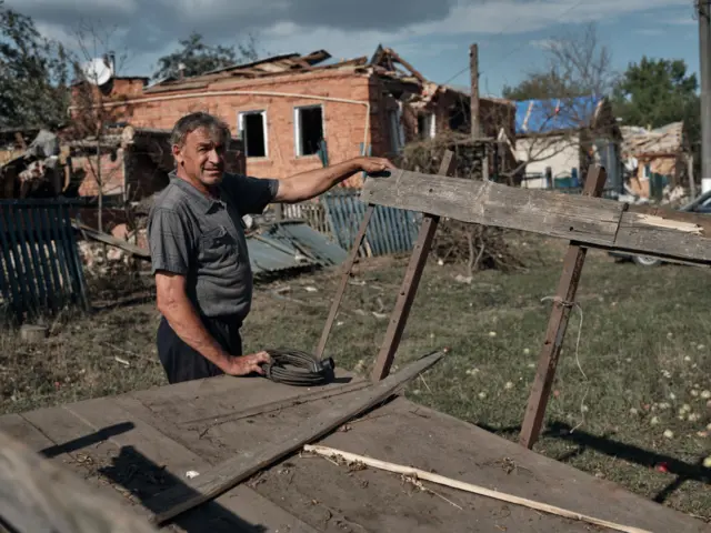 Man standing in front of damaged buildings in a border village in the Sumy region