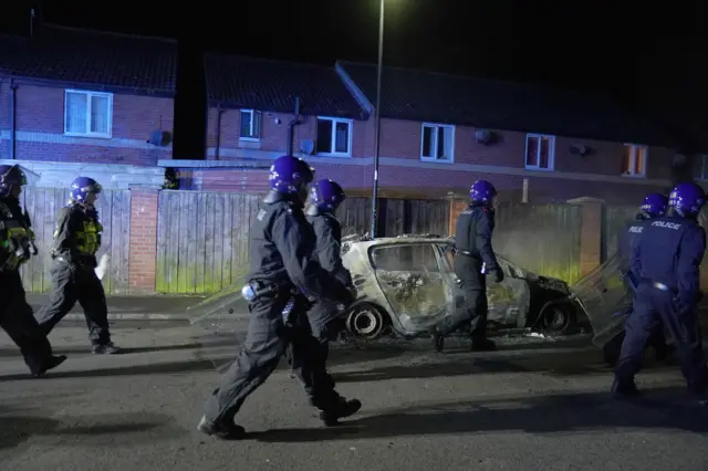 Officers walk past burnt out police vehicle