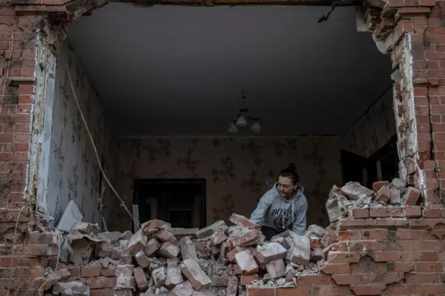 A woman inside a house with one wall that has collapsed