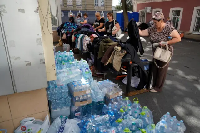 People looking at a pile of clothes and a large collection of water bottles at humanitarian collection points