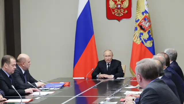 Russian President Vladimir Putin sits at the head of a long table, chairing a meeting with security council members