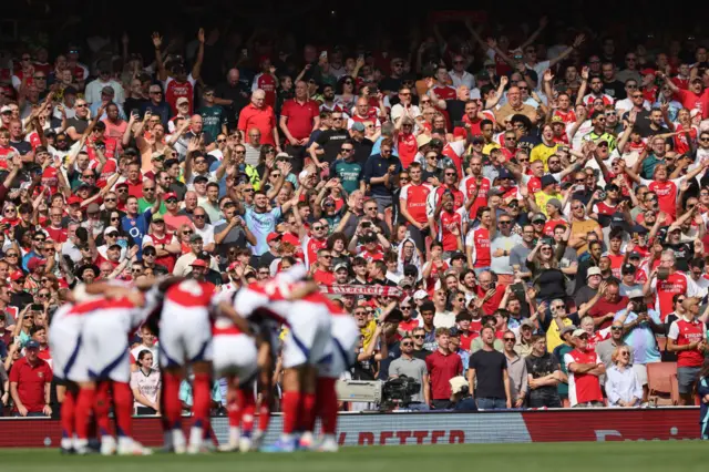 Atrsenal players huddle before kick off as fans cheer from the stands