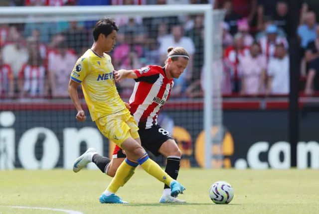 Daichi Kamada of Crystal Palace passes the ball while being challenged by Mathias Jensen of Brentford