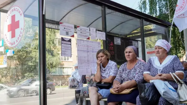 Women wait near a bus stop as the resettlement of residents from the Kursk order areas continues