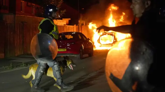 A police car burns and officers in riot gear are deployed in Hartlepool.