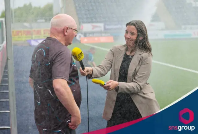 John McGlynn and Amy Canavan being soaked by sprinklers during the pre-match interviews