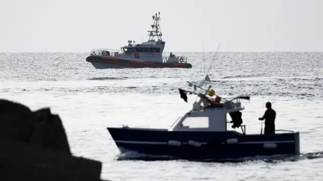 A fishing boat sails past a coast guard vessel operating in the sea to search for the missing