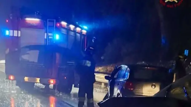 In a photo streaked with rain, a fire engine is parks on a road as firefighters approach a small car