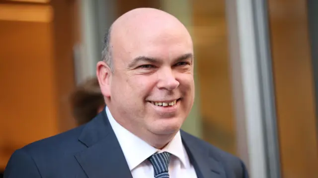 Mike Lynch smiling while wearing blue suit with plain shirt and patterned blue tie