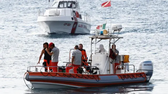 Six men stand on a small orange boat on the water