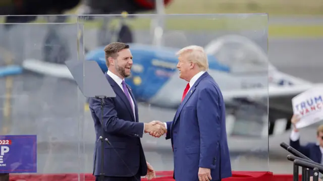 Donald Trump and JD Vance shake hands behind bullet-proof glass