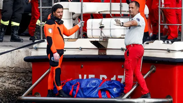 Two divers either side of a blue body bag on rescue boat at port of Porticello