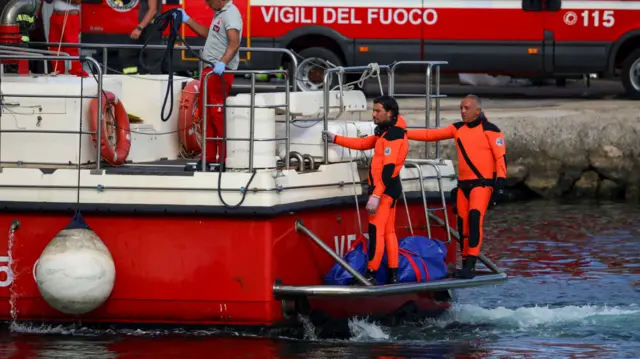 Two divers either side of a blue body bag on rescue boat at port of Porticello