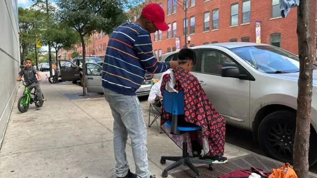 In Chicago, a migrant cuts hair on the side of the street