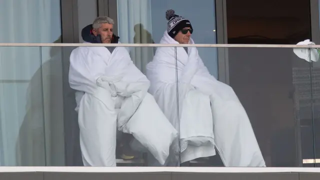 Spectators wrapped in duvets watching the cricket from a balcony at Old Trafford