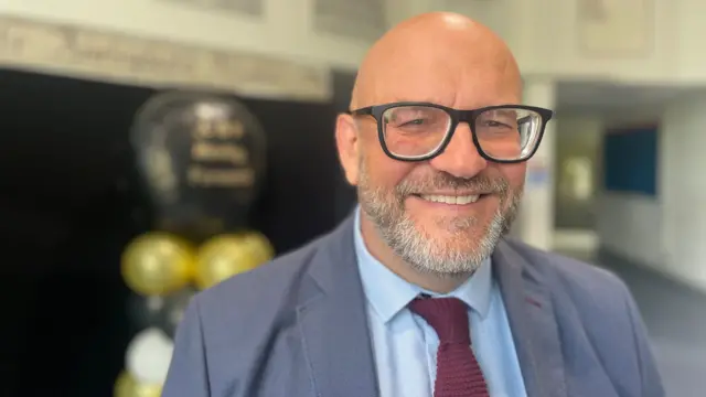 Head teacher Chris Parry looking into the camera smiling, wearing a suit and glasses