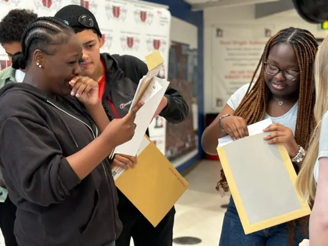 On the left, a girl with braids wearing a fleece has her hand to her mouth and is smiling at her results sheet, as a male student in the background points at it. On the right, another student wearing glasses is opening her own results.