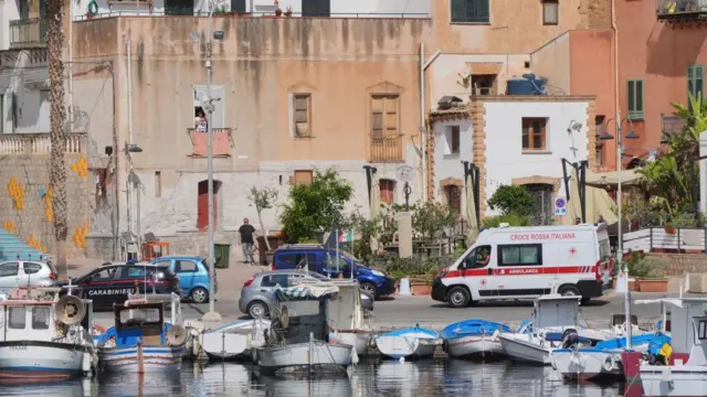 A police car escorts an ambulance carrying the fifth body recovered from Porticello Harbour, on the fourth day of the search for the six tourists missing after the luxury yacht Bayesian sank in a storm on Monday whilst moored around half a mile off Porticello on the Sicilian coast