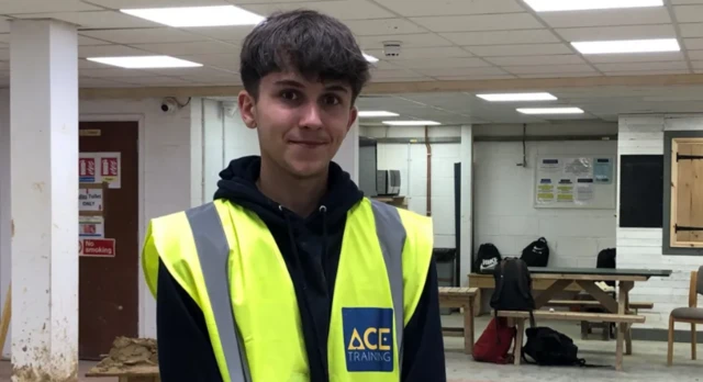 A boy in a classroom wearing a hi-vis jacket