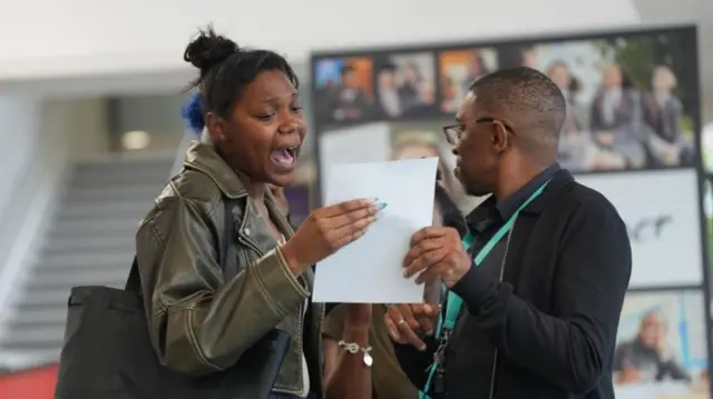 A girl celebrates her GCSE results, she and her teacher are holding a piece of paper