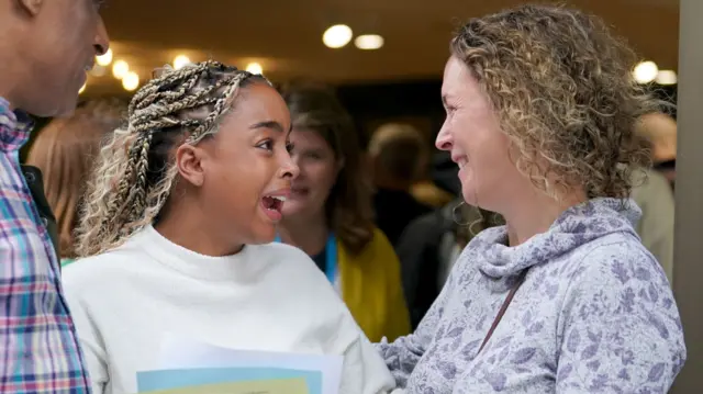 Girl holds piece of paper with look of joy in her face as she turns to a woman