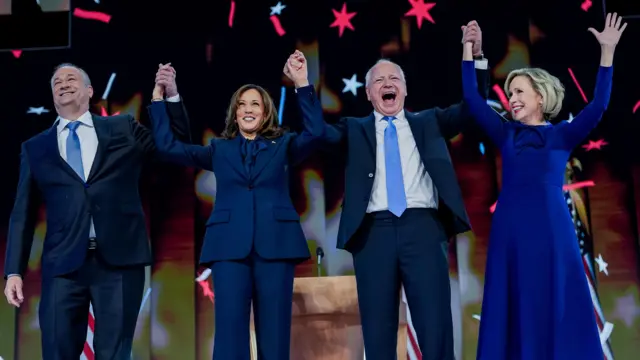 Kamala Harris, Doug Emhoff, Tim Walz and his wife Gwen Walz hold hands as they stand together on stage