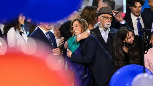 Kamala Harris hugs people on stage as a sea of balloons fill the convention floor