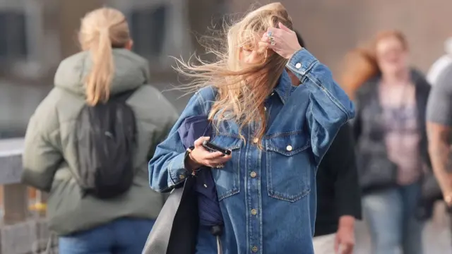 Woman wearing a denim jacket tries to move her hair out her face from the wind