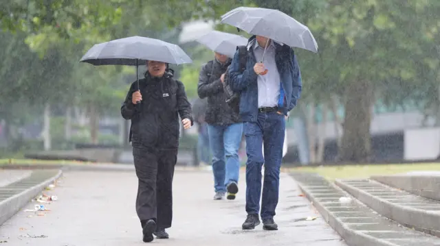 Three people walk along holding umbrellas