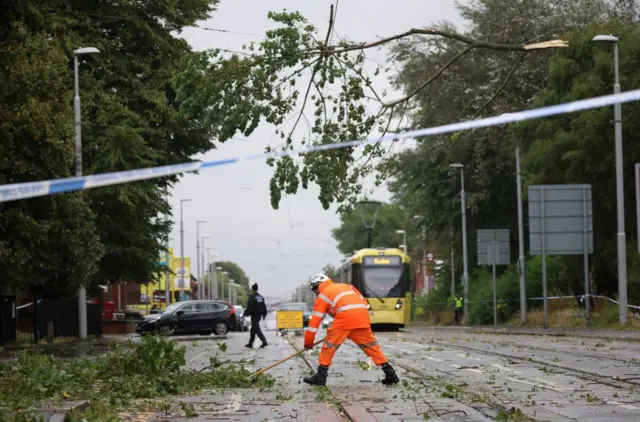 A worker begins to remove fallen tree branches after strong winds brought by Storm Lilian brought down trees blocking roads and tram routes in Manchester