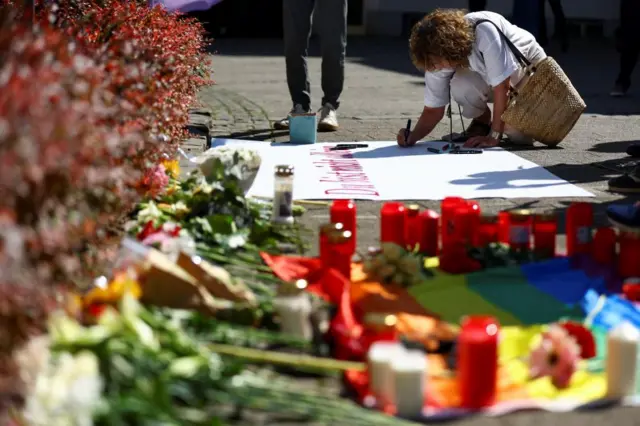 A woman writes on a placard near tributes placed on the ground following an incident in which several individuals were killed after a man randomly stabbed passers-by with a knife at a city festival, in Solingen