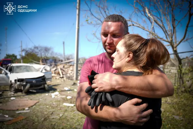 Local residents embrace each other at the site of a Russian missile strike