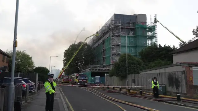 Building in Dagenham is seen after a fire broke out. Smoke is billowing from the top of the building as officers standby.