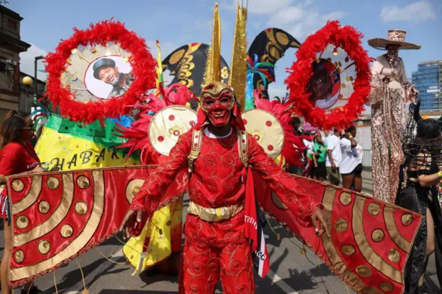 A man in a red costume in front a float at Notting Hill carnival