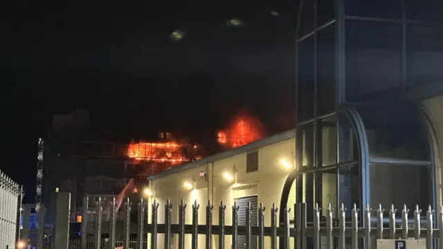 A building in east London is seen from afar and it is on fire as flames blaze above it.