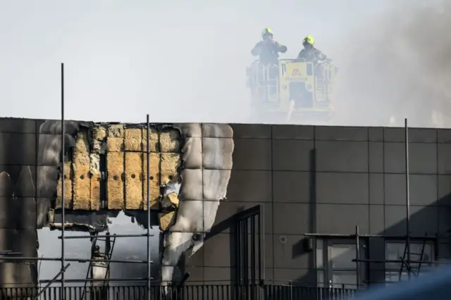 Exposed cladding is seen as fire teams attempt to extinguish a major fire in an apartment block