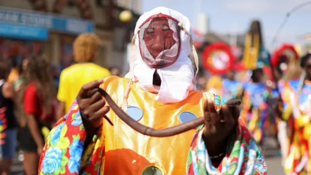 A person in a colourful costume with their face hidden, holding a snake.