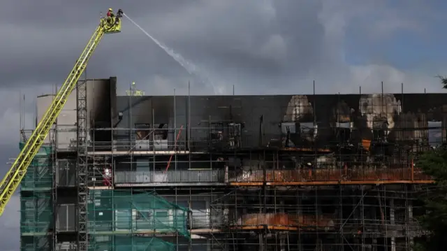 Firemen on an aerial ladder direct a hose onto a Dagenham tower block blackened by a fire