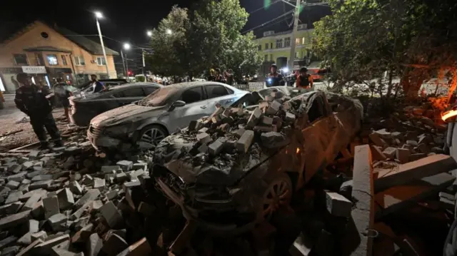 Rubble lies on top of cars with one onlooker