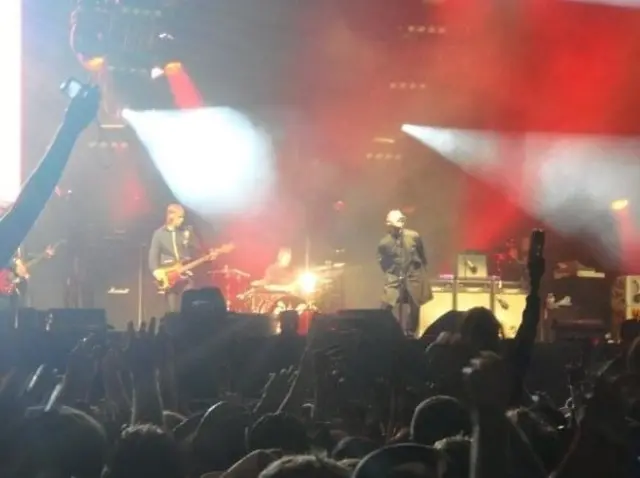 Noel and Liam Gallagher on stage at V Festival in 2009. Noel on the left playing guitar and Liam on the right singing into microphone with his hands behind his back as audience stand in front of the stage waving their hands