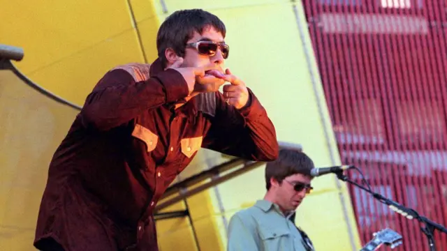 Oasis brothers perform on stage and stick out their tongues at fans