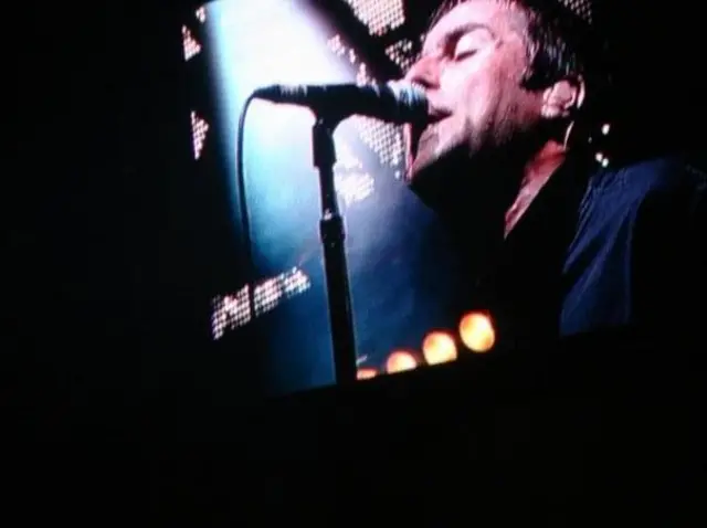 Liam Gallagher on stage at V Festival close up image of him singing into microphone taken from audience