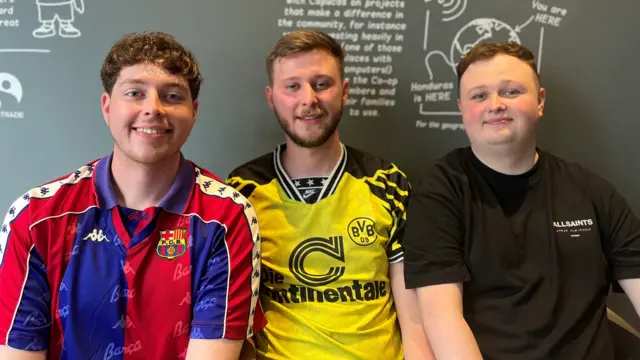 Three men sat in front of a blackboard. From left to right they wear a Barcelona football shirt, a Borussia Dortmund shirt and a black t-shirt