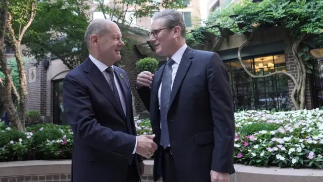 Keir Starmer and Olaf Scholz meeting in Washington DC both in dark suits and ties surrounded by flower beds and a building with a tree growing up the wall and onto the ceiling