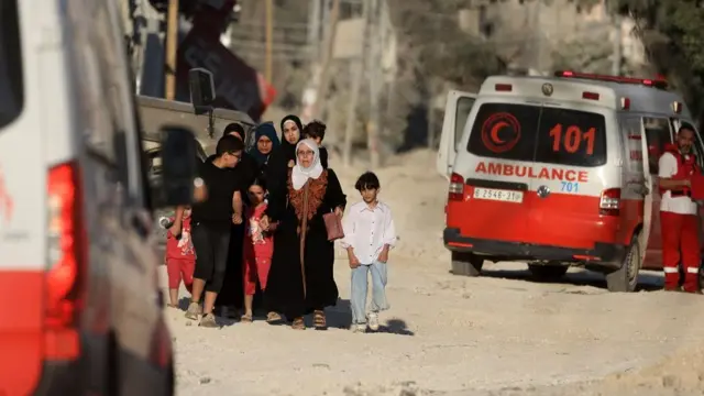 Members of a Palestinian family fleeing an Israeli raid in the Nur Shams camp near the city of Tulkarem in the Israeli-occupied West Bank, walk past Red Crescent ambulances stationed outside the camp on August 28, 2024