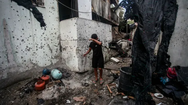 Child walks through rubble left on street in Nur Shams camp in Tulkarm as debris lies on the floor, nearby walls are covered in holws and fabric drapes from the building ripped up