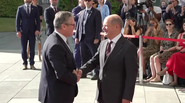 Keir Starmer greeting German Chancellor Olaf Scholz in suits as crowd look on