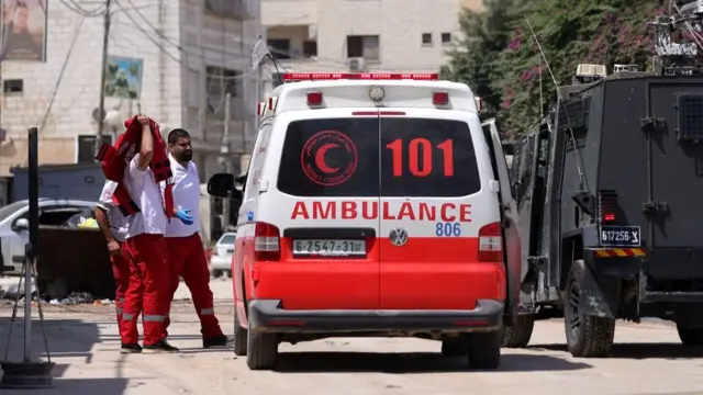 A worker of the Palestine Red Crescent Society takes off his vest as they are body-searched by the Israeli army (R) during a military operation outside a hospital in the West Bank city of Jenin, 28 August 2024